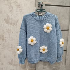 a blue sweater with white and yellow flowers is hanging on a rack in front of a door