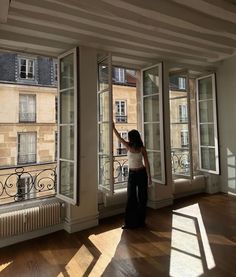 a woman standing in an empty room looking out the window