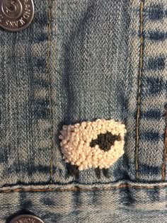 there is a small sheep in the pocket of a jean jacket with buttons on it