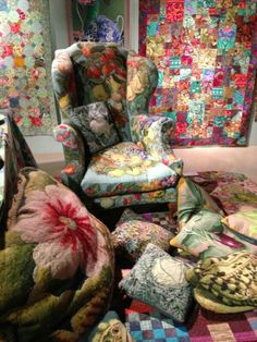 an upholstered chair is surrounded by quilts and pillows in a room with wallpapered walls