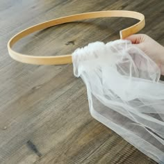 a person is holding a piece of white tulle on a wooden table with a headband