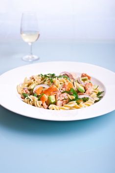 a white plate topped with pasta and veggies next to a glass of wine