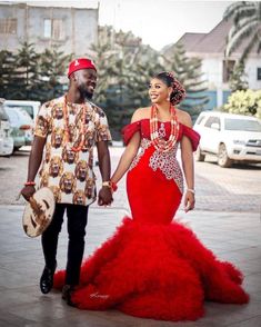 a man and woman dressed in red walking down the street with cars parked behind them