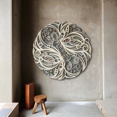 an intricately designed wall hanging on the side of a gray wall next to a wooden stool