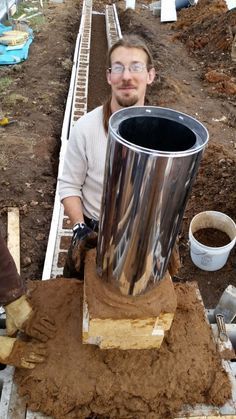 a man standing next to a large metal cup on top of a pile of dirt