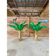 two fake palm trees sitting in front of a wooden wall