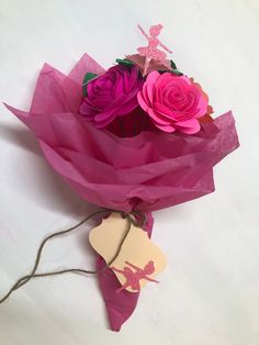 a bouquet of pink roses wrapped in purple tissue paper with a tag attached to it