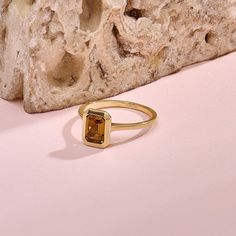 a gold ring sitting on top of a pink surface next to a rock and stone wall