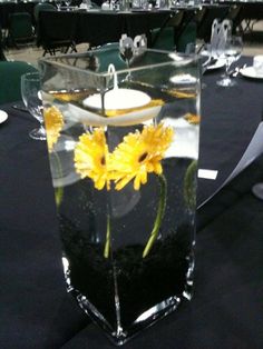 a vase filled with water and yellow flowers on top of a black tablecloth covered table