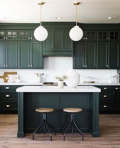 a kitchen with dark green cabinets and white counter tops, two stools at the island