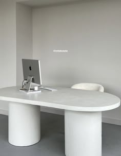 a white table with a computer on it in an empty room next to a chair