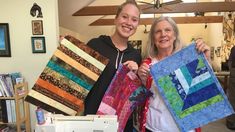 two women holding up quilts in a room