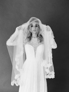 black and white photo of woman in wedding dress with veil over her head, looking at camera