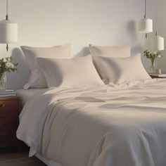 a bed with white sheets and pillows in a bedroom next to two lamps on either side of the bed