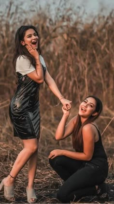 two women are laughing and holding hands in front of some tall dry grass while one holds the other's hand