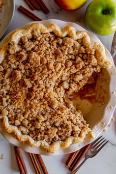 an apple pie on a white plate with cinnamon sticks and apples in the back ground