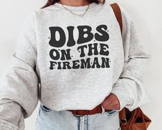 a woman wearing a sweatshirt with the words dibs on the fireman printed on it