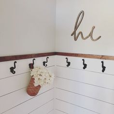 there is a vase with flowers in it on the wall next to hooks and letters