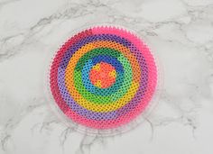 a circular object made out of plastic beads on a marble counter top with a rainbow colored circle in the middle