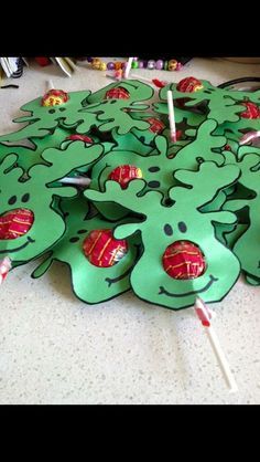 a bunch of green paper cut outs with candy in them on the floor next to some lollipop sticks