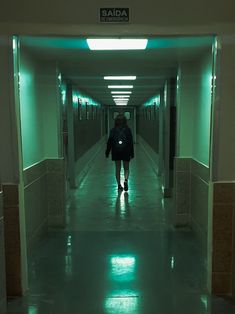 a person walking down a long hallway with green lights on either side of the corridor