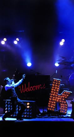 a man standing on stage in front of a sign that reads welcome to kk