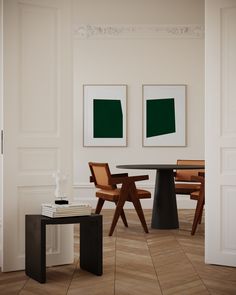 two paintings hang on the wall next to a table and chairs in a room with parquet flooring