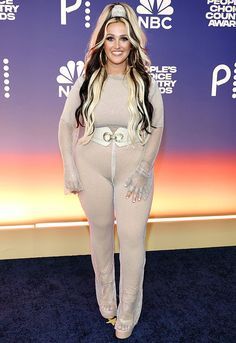 a woman in a bodysuit posing on the blue carpet at an awards event with her hands behind her back