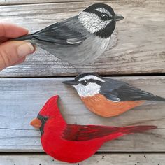 three birds painted on wooden boards with one being held up to the side by someone's hand