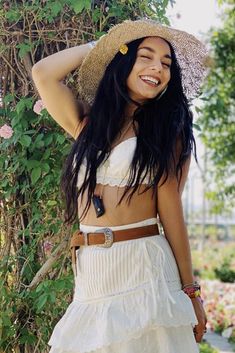 a woman in a white dress and straw hat posing for the camera with her arms behind her head