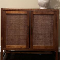 a wooden cabinet with two doors and a white vase on it's top shelf