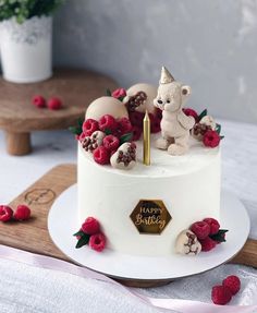 a birthday cake decorated with raspberries and a teddy bear