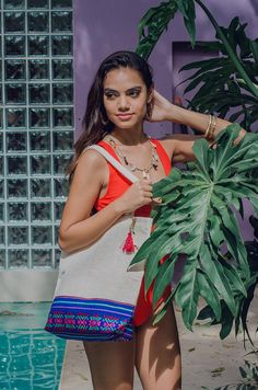 a woman standing next to a pool with a plant in her hand and wearing an orange top