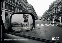 a rear view mirror reflecting a man's face on the side of a street