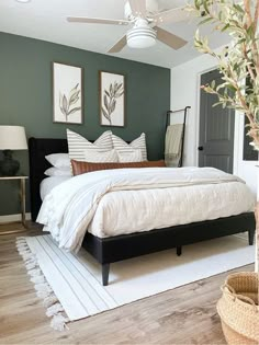 a bedroom with green walls and white bedding, wooden flooring, two framed pictures on the wall