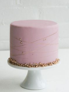 a pink cake with gold sprinkles on top sitting on a white pedestal