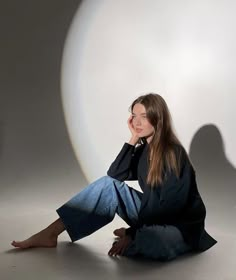 a woman sitting on the ground in front of a white ball with her hands behind her head