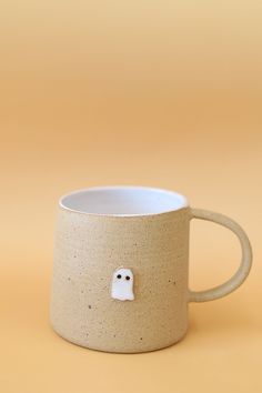 a ceramic mug with a ghost face on it's side and a yellow background