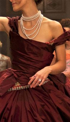 a woman in a red dress with pearls on her neck and necklace, sitting down