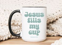 a coffee mug with the words jesus fills my cup on it sitting next to a pile of blankets