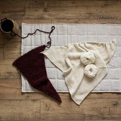 two knitted items are laying on the floor next to a cup of coffee