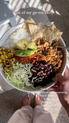 someone is holding a bowl full of mexican food with their feet on the floor next to it