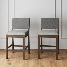 two chairs sitting next to each other on top of a hard wood floor in front of a white wall