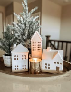 small white houses on a tray with a candle in front of them and a christmas tree