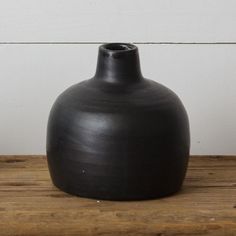 a large black vase sitting on top of a wooden table next to a white wall