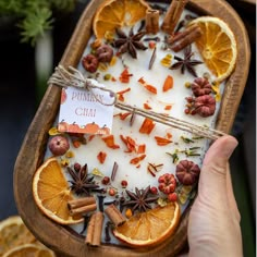 a person holding an orange slice with cinnamons and star anise on it in a tray