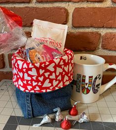 a red and white basket filled with candy next to a coffee mug