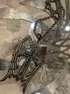 Large cross with wings Plated in black  with hematite  colored  Crystals. It is hypoallergenic and comes on a 20inch chain. Cross With Wings Necklace, Cross Jewelry Gold, Aesthetic Cross Necklace, Angel Wing Jewelry, Villain Jewelry, Gothic Cross Necklace, Alt Accessories, Cross With Wings, Chains Aesthetic