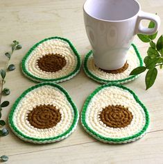 four crocheted coasters sitting on top of a table next to a cup