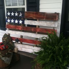 an american flag made out of pallet wood sitting on the front porch next to a potted plant